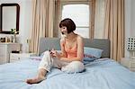 Young woman sitting on bed looking at mobile phone