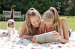 Two teenage girls on picnic blanket looking at digital tablet
