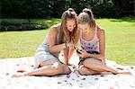 Two teenage girls on picnic blanket looking at mobile phone