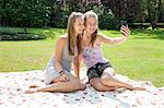 Two teenage girls on picnic blanket taking self portrait