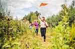Four young women running through scrubland with kite