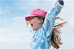 Girl wearing pink cap with arms raised in wind