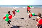 Mother with four childen on beach with balloons, Wales, UK