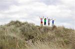 Four friends on dunes with arms out, Wales, UK