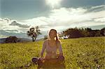 Young woman sitting cross legged in field daydreaming