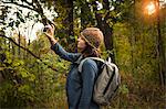 Mature woman taking photograph in forest using smartphone