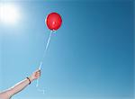 Hand holding single red balloon against blue sky