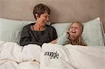 Mother and daughter laughing in bed