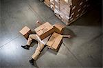 Man lying on floor covered by cardboard boxes in warehouse