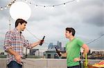 Two male adult friends chatting at rooftop barbecue