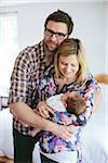 Portrait of Mom and Dad holding newborn, baby boy standing in bedroom, USA