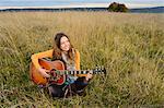 Smiling young woman playing guitar in field