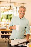 Senior man drinking coffee and reading newspaper in kitchen