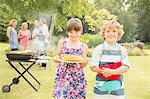 Brother and sister holding grilled corn near barbecue in backyard