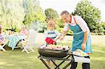 Grandfather and grandson grilling meat and corn on barbecue