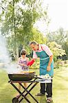 Grandfather and granddaughter grilling at barbecue in backyard