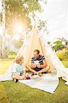 Father and son using digital tablet in teepee in backyard