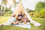 Father and children relaxing in teepee in backyard