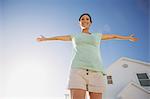 Woman smiling with arms outstretched against blue sky