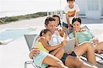 Family using digital tablet on lounge chair at poolside