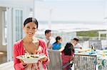 Woman holding salad bowl on sunny patio overlooking ocean