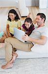 Father and daughters using laptop on sofa in living room