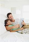 Father and son using digital tablet on bed