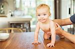 Father helping baby crawl on table