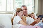 Father and children using digital tablet on bed