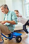 Boy pushing father on tricycle indoors