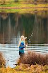 beautiful blond girl fishing in pond at autumn