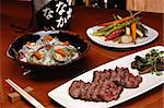 Deliciously displayed slices of Kobe Beef Filet Mignon.  Topped with sea salt and garnished with an arugula and pickled shiitake mushroom salad.  Beside it a vegetable dish and wood roasted oysters.