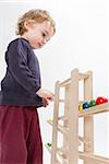 young child playing with wooden ball path. studio shot in grey background