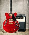 red semi-hollow electric guitar and amplifier on brown canvas background