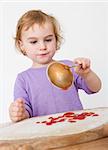 child putting sieved tomatoes on dough. studio shot in grey background