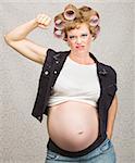 Young pregnant woman in curlers flexing her biceps