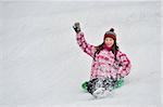 Happy girl sliding on sled with her hands lifted in the mountains