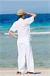 Back view a man with looking out gesture in a white suit and hat standing on a tropical beach