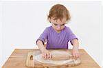 cute curly child rolling out dough. studio shot in grey background