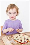 young child putting cheese on homemade pizza. studio shot with light grey background