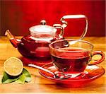 A cup of warm tea with teapot in background on a wooden desk