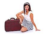 Retro style woman sitting on the floor near an old suitcase, posing to camera over white background.