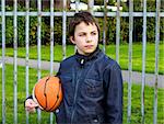 young basketball player holding ball against iron fence at the playground