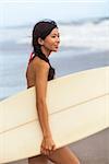 Beautiful Hawaiian Asian young woman surfer girl in bikini with surfboard looking at the waves on a sunny beach