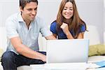 Cute young couple sitting on sofa and using laptop at home