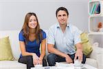 Portrait of a smiling young couple with bills sitting in living room at home