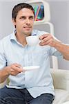 Thoughtful young man drinking tea in living room at home