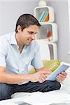 Smiling young man with bills using digital tablet in the living room at home