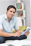 Portrait of a smiling young man with bills using digital tablet in the living room at home
