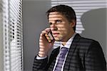 Serious young businessman peeking through blinds while on call in the office